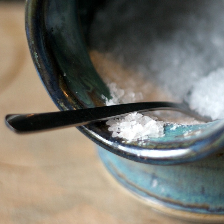 Grobes Salz auf einem Löffel in einem Tonkrug
